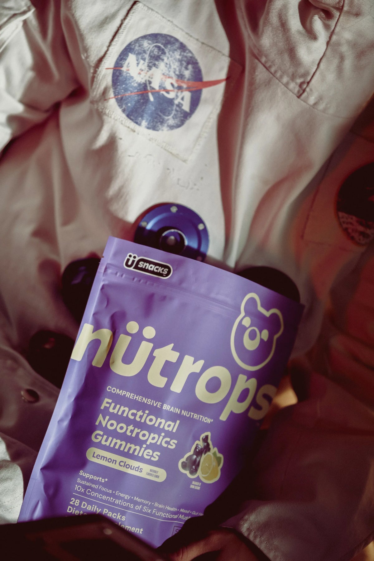 A person in an orange jumpsuit holds up a purple pouch of nütrops gummies inside a spaceship.